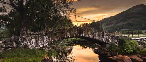A stone bridge over a calm river with a sunset in the background.