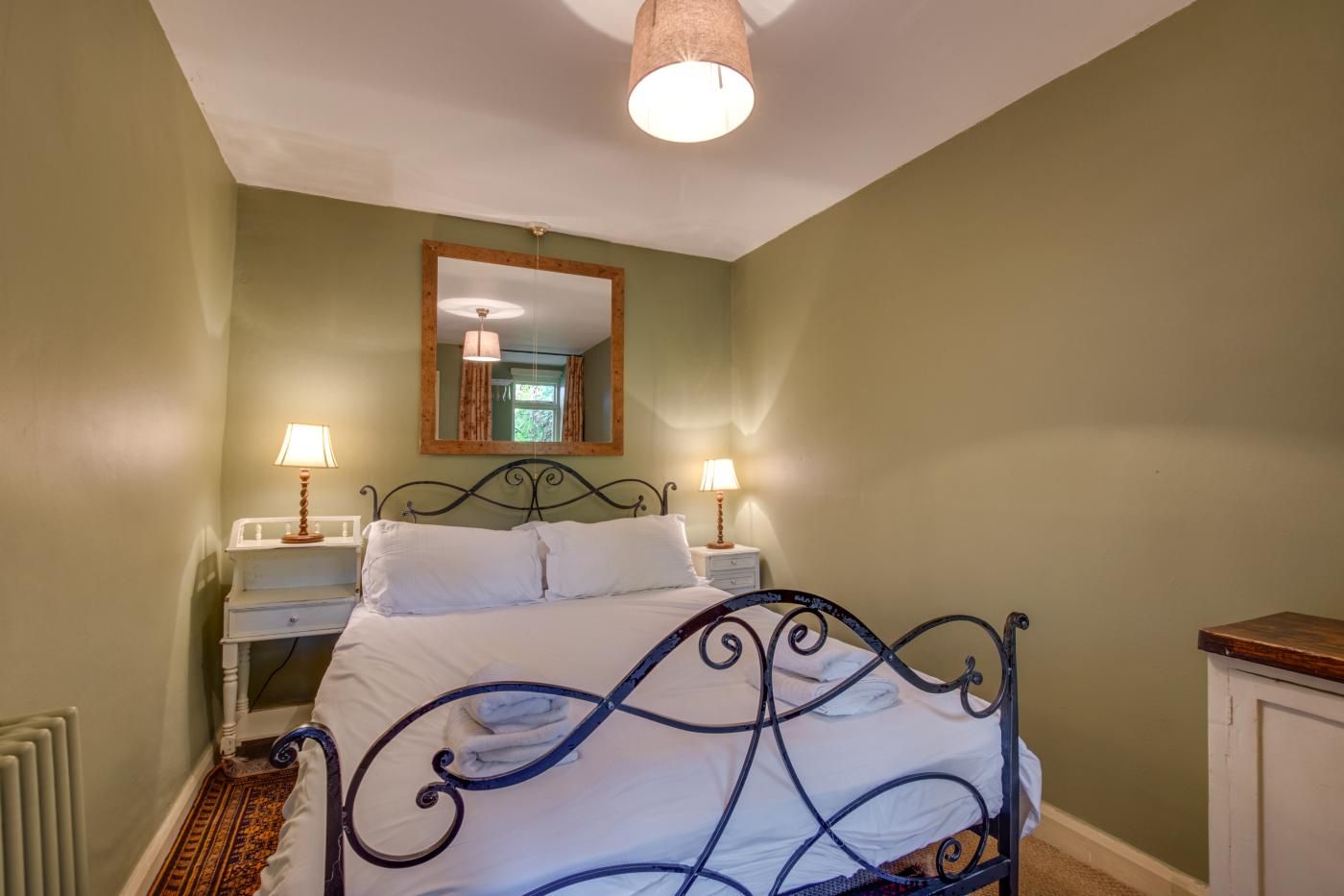 A bedroom with a bed, bedside tables, a mirror, and a hanging light fixture.