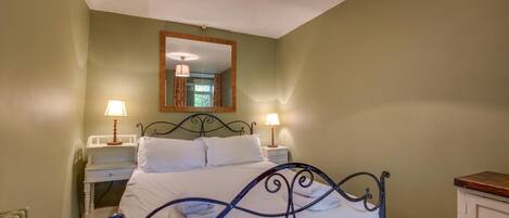 A bedroom with a bed, bedside tables, a mirror, and a hanging light fixture.