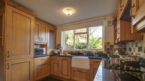 A kitchen with wooden cabinets, a black countertop, a window with a view of greenery, and a stove. - 3 Bed in Little Langdale (oc-gl102) (Little Langdale)