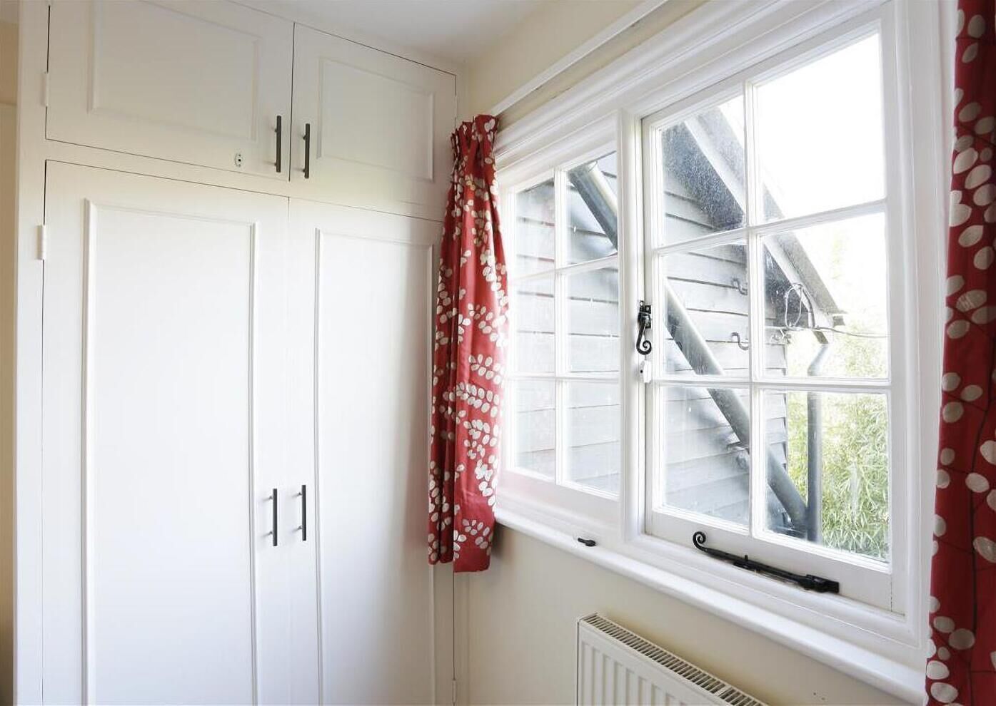 A room with white cabinets, a window with a view of a house, and a radiator below the window.