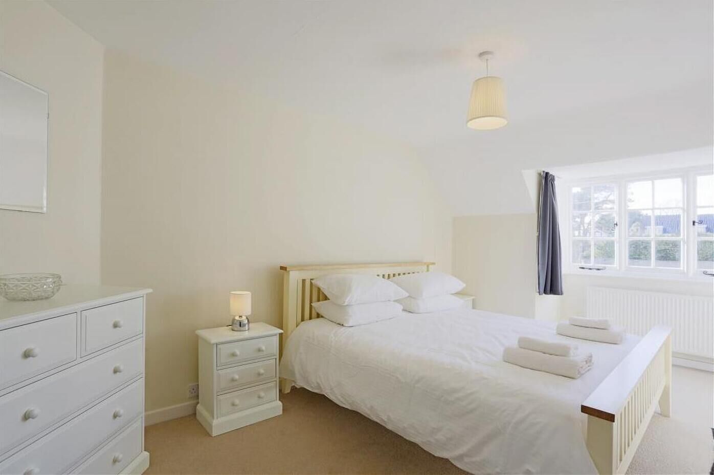 A bedroom with a bed, bedside table, dresser, and a window with curtains.