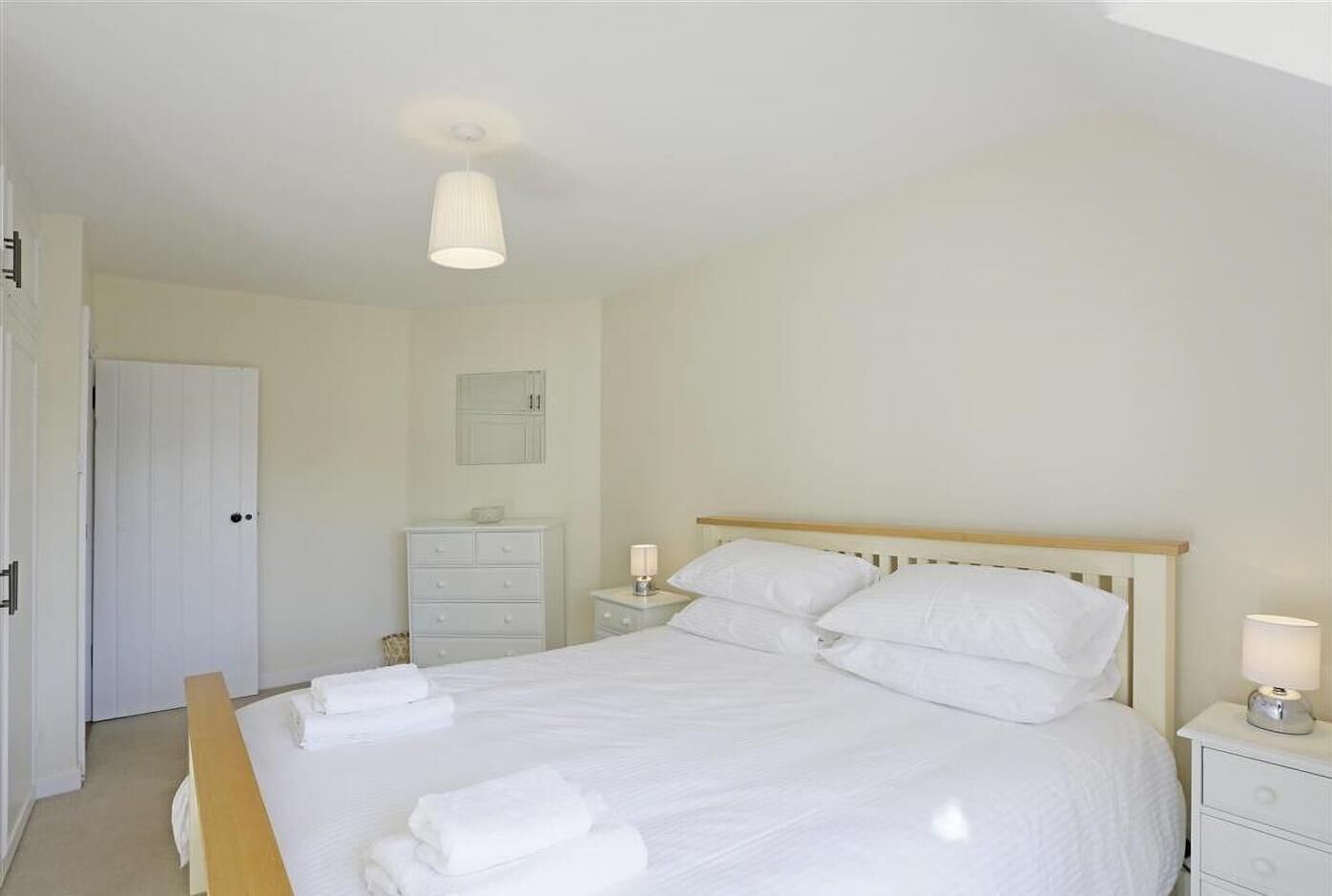 A neatly made bed with white linens, a bedside table with a lamp, and a dresser with drawers.