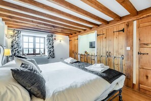 Quarto com uma cama grande, vigas de madeira no teto, uma janela com cortinas e um guarda-roupa de madeira.