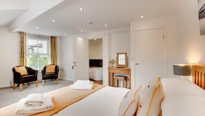 Et moderne hotelværelse med en stor seng, et siddeområde med to stole, et sminkebord med spejl og et vindue med gardiner.