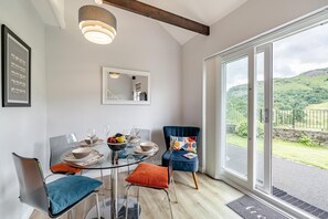 A dining area with a glass table, chairs, and a view of the countryside through large windows. - 2 Bed in Chapel Stile (oc-gl103) (Chapel Stile)