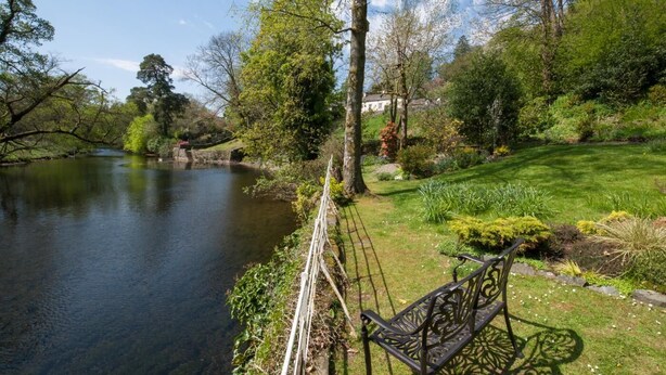 Un jardin au bord de la rivière, avec un banc et un mur en pierre.