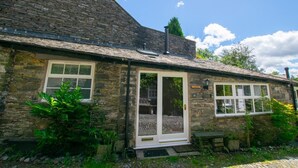 Une petite maison en pierre avec un toit de tuiles, une porte blanche et un petit porche.