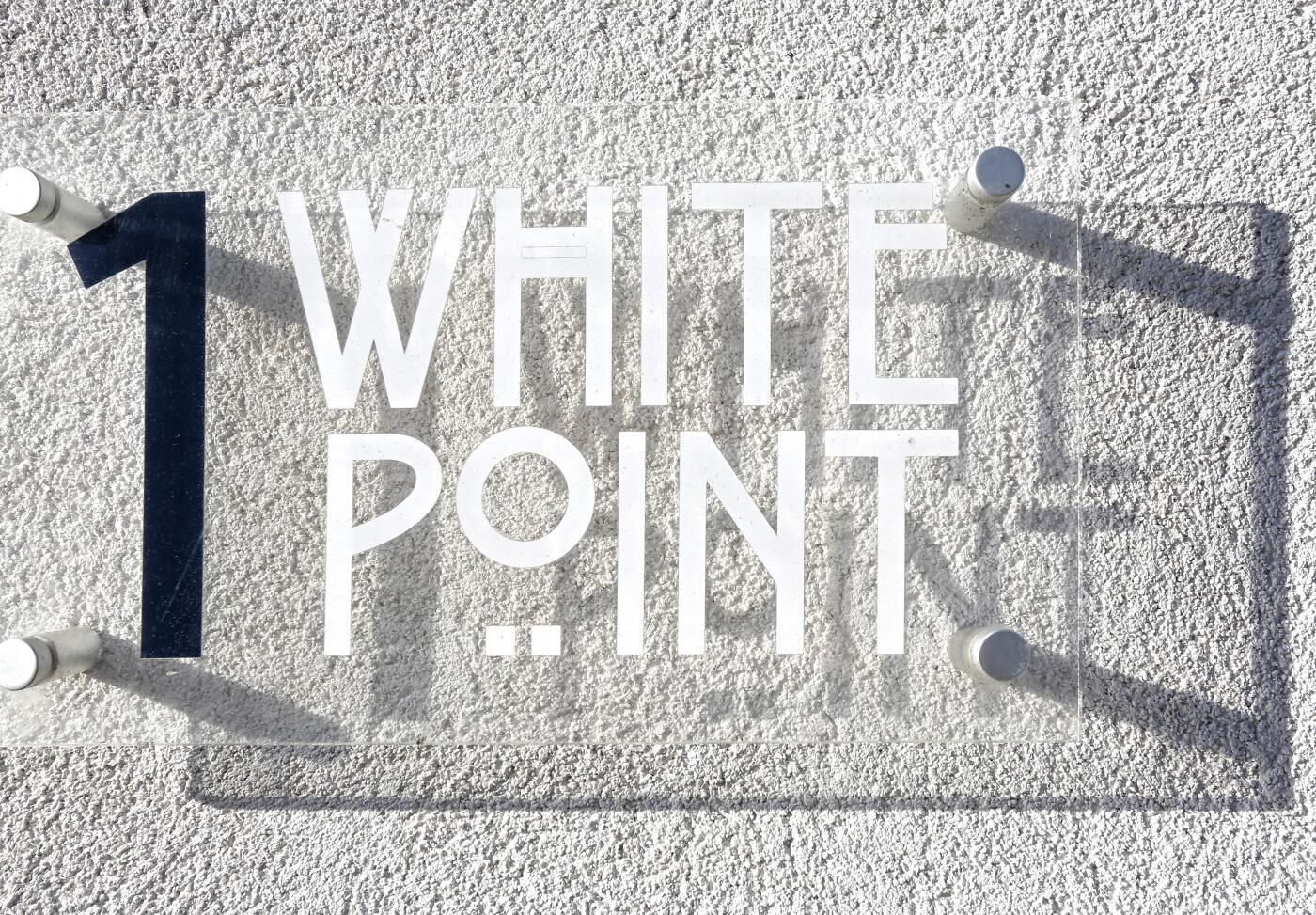A sign with the text "1 WHITE POINT" mounted on a textured wall.