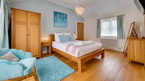 Ein Schlafzimmer mit einem hölzernen Bett, einem Nachttisch, einem blauen Sessel, einem blauen Teppich, einem Holzschrank, einem Gemälde, einer Chandelier und einem Fenster mit Vorhängen, sowie einer Heizung.