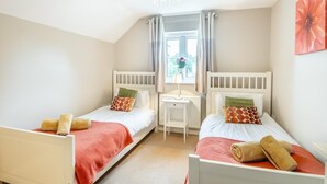Ein Schlafzimmer mit zwei Einzelbetten, einem Schreibtisch und einem Fenster mit Vorhängen.