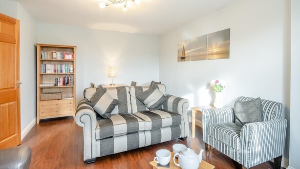Ein Wohnzimmer mit Sofa, gestreiftem Sessel, Bücherregal und einem Tisch mit Teekanne und Tassen.