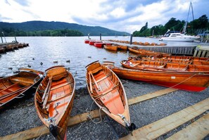 Eine Steg am Seeufer mit Holz-Ruderbooten und einer Segelyacht.