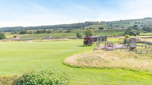 A rural landscape with a grassy field, a small building, and a fenced play area.