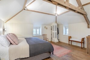 Ein Schlafzimmer mit schrägen Wänden, einem Bett mit Kissen, einem Sessel und einem kleinen Tisch.