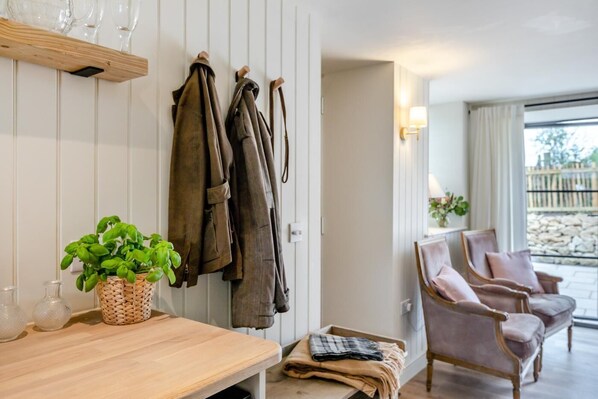Ein Zimmer mit einem Holztisch, einem Blumentopf, einer Bank, einem Stuhl und einem Kleiderständer mit Jacken.