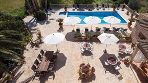 A pool area with lounge chairs and umbrellas, surrounded by stone flooring and potted plants. - Agroturismo S'Hort de Can Carrio (Ses Salines)