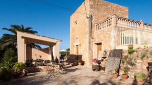 A stone building with a balcony, outdoor seating, and potted plants. - Agroturismo S'Hort de Can Carrio (Ses Salines)