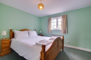 Ein Schlafzimmer mit einem hölzernen Bett, einem Nachttisch mit Lampe, einem Fenster mit Vorhängen und einer Pendelleuchte.