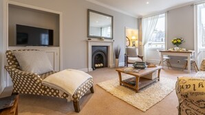 Een woonkamer met een televisie, een open haard, een eethoek met een tafel en stoelen, en een groot raam met gordijnen.