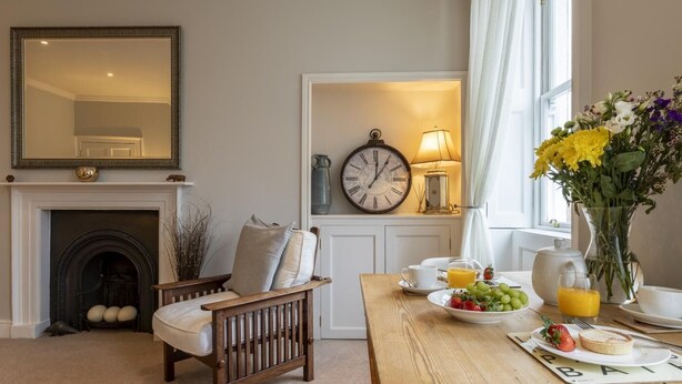 Een gezellige woonkamer met een open haard, een ontbijt gedekte eettafel, een klok en een bloemenvaas.