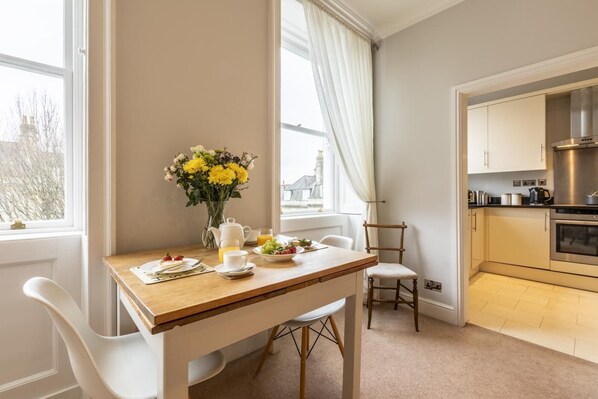 A modern kitchen with a dining area, a vase of flowers, and breakfast items on the table. - 1 Bed in Bath (oc-bhr12) (Bath)