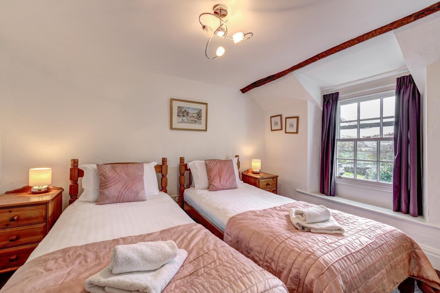 A hotel room with two beds, a window with curtains, a painting on the wall, and a ceiling light fixture.