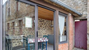 A stone building with a glass door leading to a dining area with a table and chairs. - “Chambre Champêtre” Guest Room with Shared Terrace, Garden, and Wi-Fi (Mont-Dol)