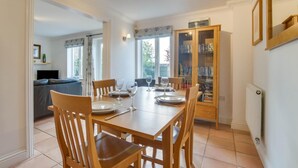 Un comedor con una mesa de madera dispuesta para cuatro personas, sillas alrededor y una estantería en el fondo.