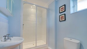 Un baño con ducha, inodoro, lavabo y dos cuadros en la pared.