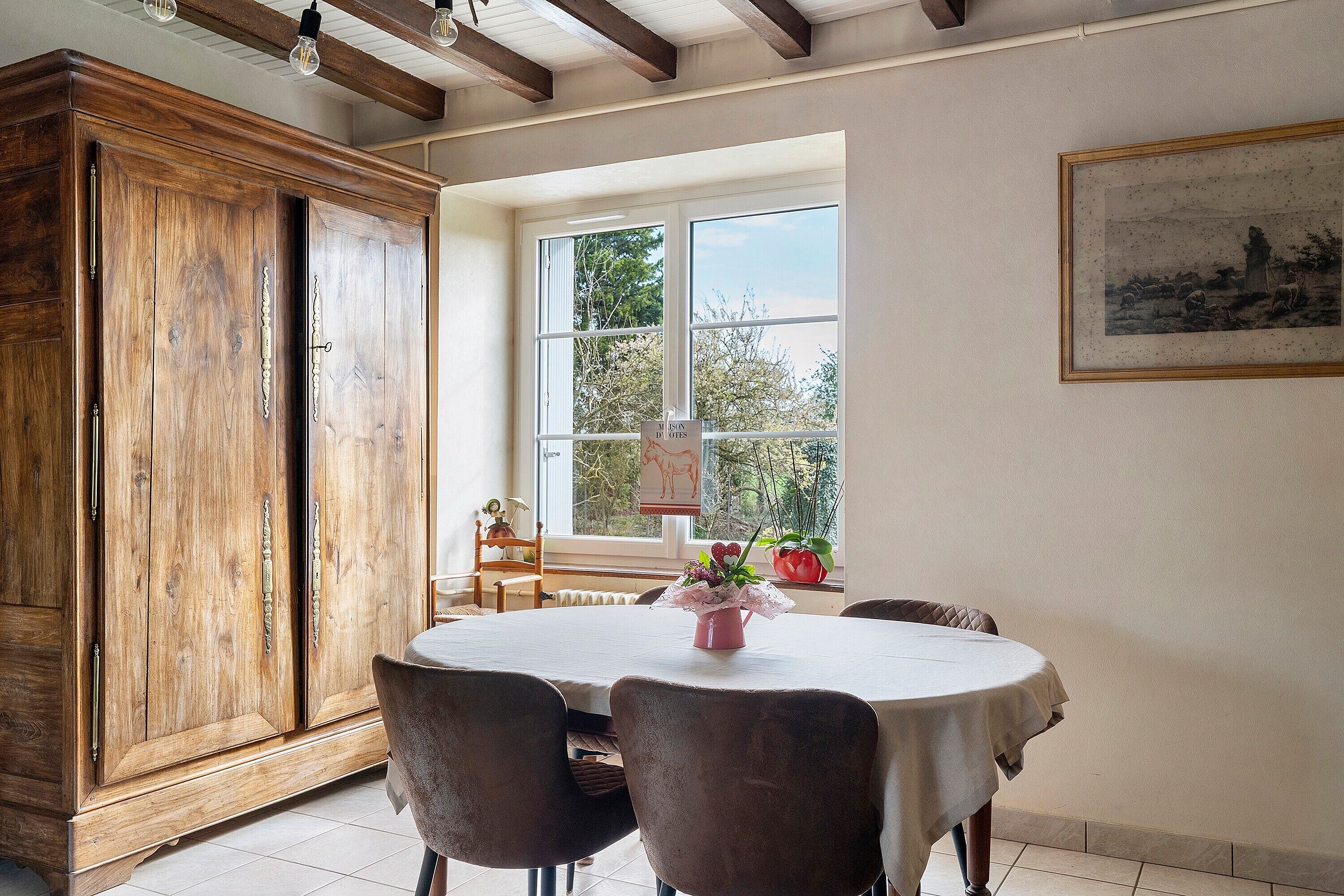 A dining area with a table, chairs, a wooden cabinet, a window with a view, and a framed picture on the wall.