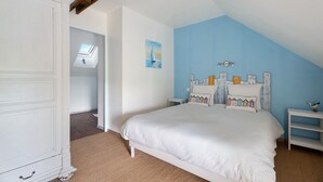 Ett sovrum med ett sluttande tak, en säng med en vit sänggavel, ett litet sängbord och en väggmonterad lampa.