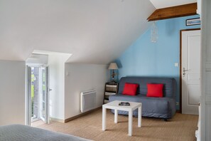 Une pièce avec un plafond en pente, un canapé avec des coussins rouges, une table blanche, une lampe et un radiateur.