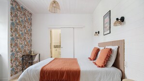 Een slaapkamer met een bed, een houten hoofdbord, een witte muur, behang met een patroon en een hangende lamp.