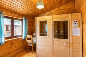 A wooden cabin interior with a wooden chair, a desk, and a window with curtains.