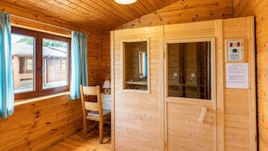 Interior de una cabaña de madera con una silla, un escritorio y una ventana con cortinas.