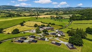 Un paisaje rural con un conjunto de edificios, incluyendo graneros y casas, rodeado de extensos campos verdes y un camino sinuoso.