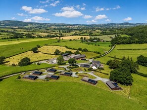 A rural landscape with a cluster of buildings, including barns and houses, surrounded by expansive green fields and a winding road.