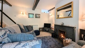 Une pièce chaleureuse avec une cheminée, une télévision et un coin salon confortable, comprenant un canapé et des coussins à motifs.