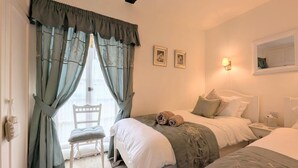 Une chambre avec deux lits, une chaise, une fenêtre avec des rideaux et une lampe fixée au mur.