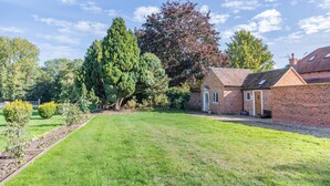 Une maison en briques avec un petit jardin, une pelouse et un grand arbre.