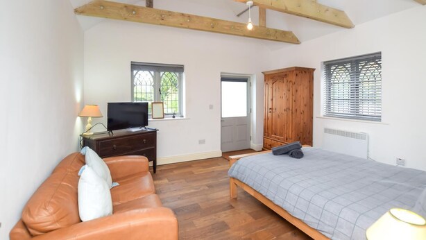 Une chambre à coucher avec un lit, une armoire en bois, un téléviseur posé sur une commode et deux fenêtres équipées de stores.