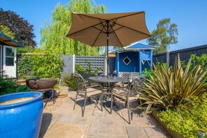 A patio with a table and chairs, a large umbrella, and a blue barrel. - 2 Bed in Aldborough (oc-2174) (Aldborough)