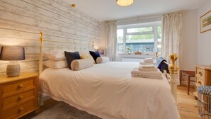 Ein großes Bett mit Holz Kopfteil, ein Nachttisch mit Lampe und ein Fenster mit Vorhängen.
