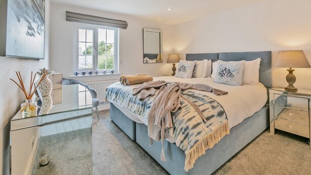 Quarto com cama grande, luminárias de cabeceira, janela e espelho.