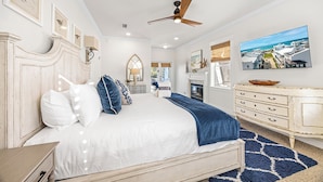 Een slaapkamer met een bed, een dressoir, een plafondventilator, een open haard en een lijst met een foto aan de muur.