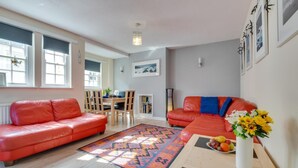 A living room with a red leather sofa, a matching armchair, a dining table with chairs, and a colorful rug.