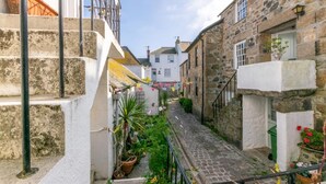 A narrow cobblestone alley with stone buildings, a staircase, and potted plants.