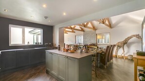 A modern kitchen with a central island, dark cabinetry, and a dining area with wooden beams and a giraffe sculpture. - 3 Bed in Newlyn (oc-s33015) (Newlyn)