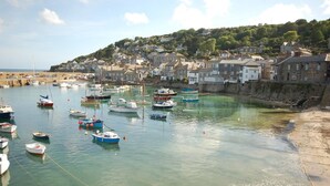 A coastal town with boats docked in a harbor, houses along the shore, and a hill in the background. - 3 Bed in Newlyn (oc-s33015) (Newlyn)
